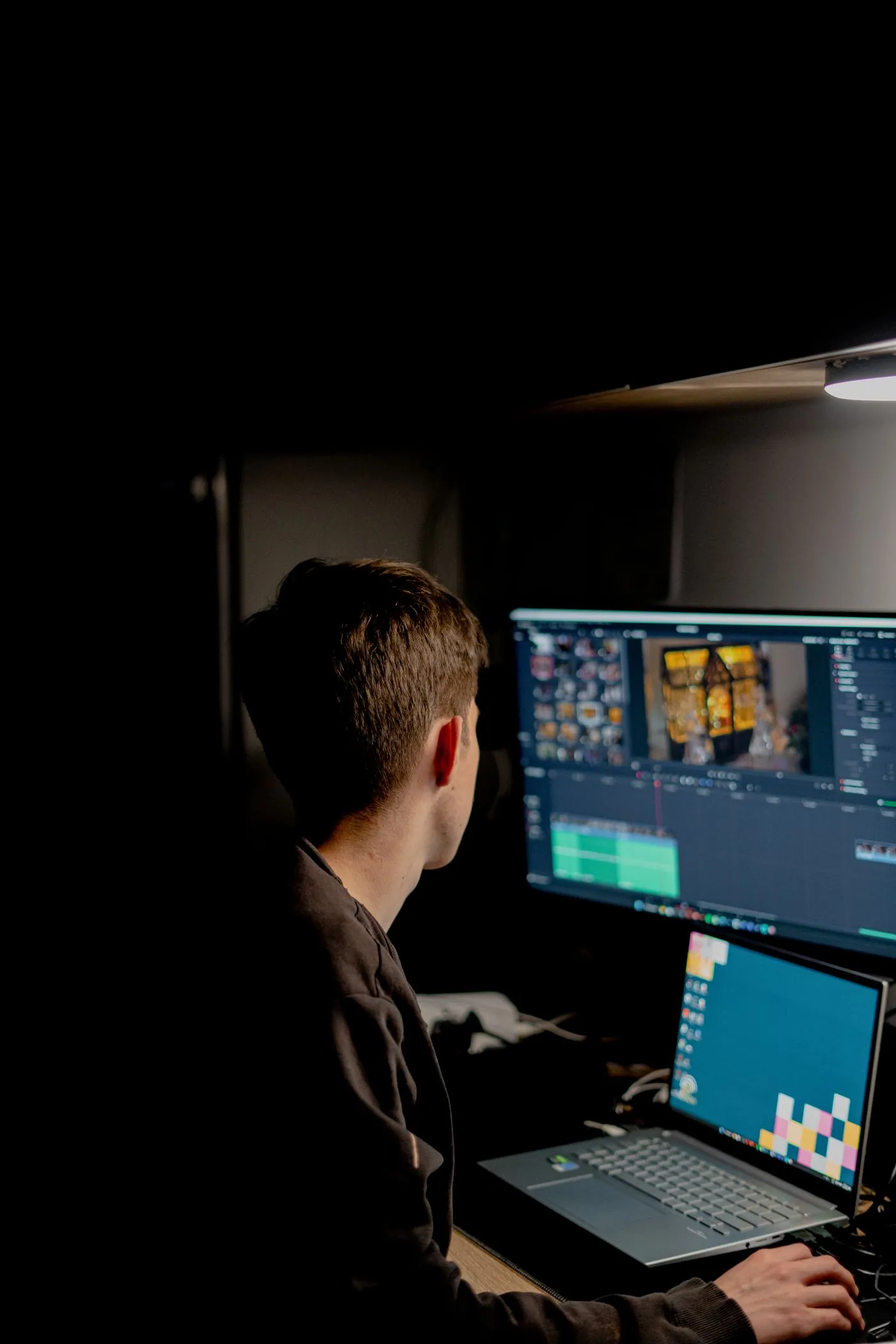 A person working with video on two screens in a dark editing room